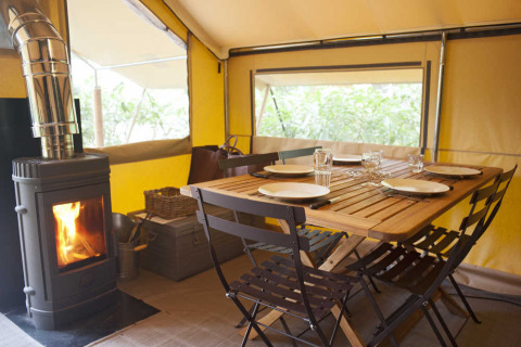 Dining table set with plates and glasses inside a cozy safari tent interior with wood stove.