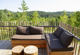 Buitenlounge op het terras van een safaritent met houten banken en uitzicht op groene bossen.