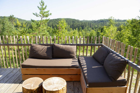 Coin salon extérieur sur la terrasse d’une tente safari avec meubles en bois et vue sur la forêt verdoyante.