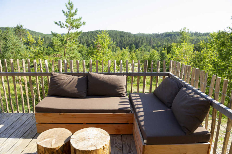 Zona de estar al aire libre en la terraza de una tienda safari con muebles de madera y vista al bosque.