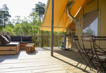 Terrasse extérieure d'une tente safari avec sol en bois, salon, table à manger et vue sur la forêt.
