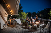 Three people sharing drinks on the lit terrace of a safari tent, enjoying a summer night outdoors.