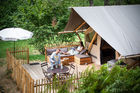 Twee mensen ontspannen op het terras van een luxe safaritent, omgeven door groene natuur.