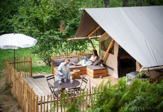 Deux personnes se détendent sur la terrasse d’une tente safari, entourées de verdure luxuriante.