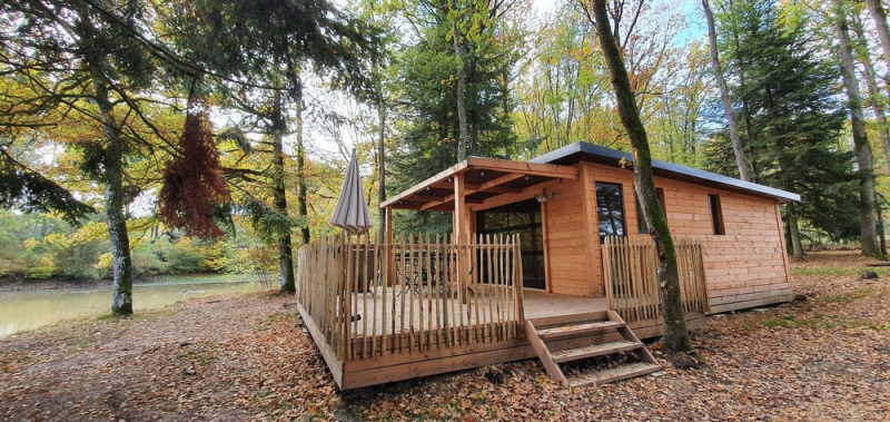 Cabaña Chalet Toronto en madera, Village Huttopia Pays de Condrieu, Francia, rodeada de bosque otoñal.