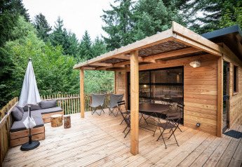 Houten terras bij Chalet Toronto, Village Huttopia Pays de Condrieu, Frankrijk, omgeven door groene bomen.