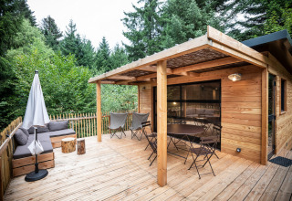 Holzterrasse des Chalet Toronto im Village Huttopia Pays de Condrieu, umgeben von Bäumen, Frankreich.
