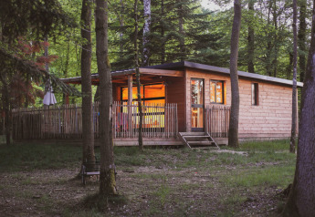 Chalet Toronto houten lodge met warme verlichting in het bos bij Village Huttopia Pays de Condrieu, Frankrijk, bij schemering.