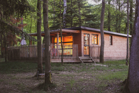 Blockhaus Chalet Toronto mit warmem Licht im Wald im Village Huttopia Pays de Condrieu, Frankreich, am Abend.