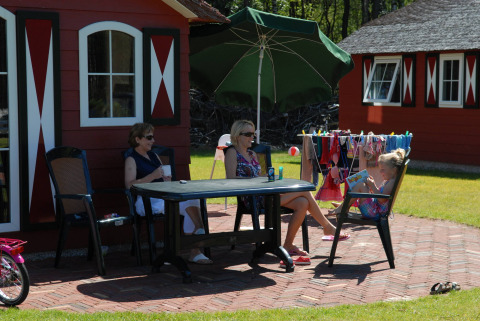 Dos mujeres y una niña sentadas en una mesa frente a una casa roja en Veluwecamping De Pampel, Gelderland, Países Bajos.