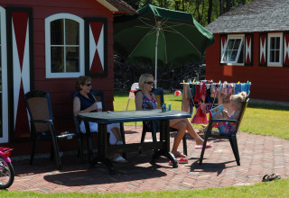 Twee dames en een meisje aan tafel voor een rood huis op Veluwecamping De Pampel, Gelderland, Nederland.