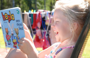 Niña sonriente lee un libro infantil al aire libre en Veluwecamping De Pampel, Gelderland, Países Bajos.