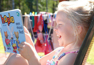 Bambina sorridente legge un libro per bambini all'aperto a Veluwecamping De Pampel, Gelderland, Paesi Bassi.