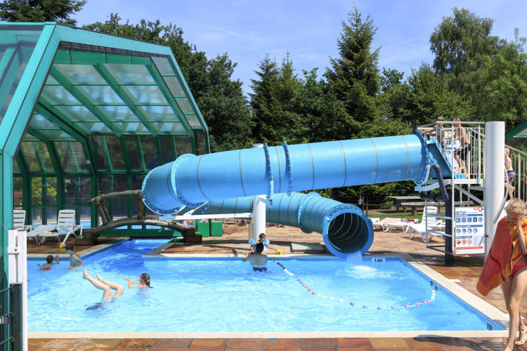 Außenpool mit blauer Wasserrutsche bei Veluwecamping De Pampel, einem Ferienpark in Gelderland, Niederlande.