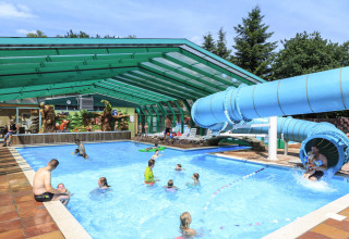 Piscina coperta con scivolo d'acqua e bambini che giocano al Veluwecamping De Pampel, Gelderland.