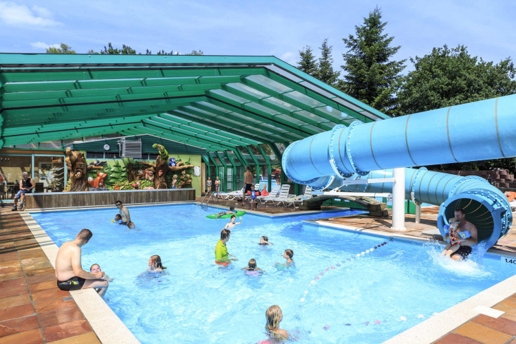 Überdachtes Schwimmbad mit Rutsche und spielenden Kindern im Ferienpark Veluwecamping De Pampel.