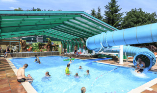 Piscina cubierta con tobogán de agua y familias divirtiéndose en Veluwecamping De Pampel en Gelderland.