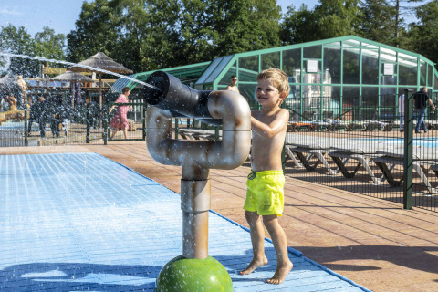 Niño con pantalones cortos amarillos juega con un cañón de agua en Veluwecamping De Pampel, Gelderland, Países Bajos.