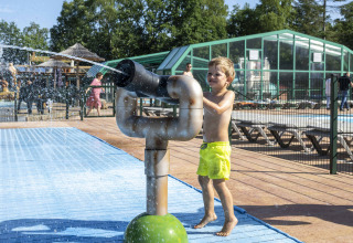 Junge in gelber Badehose spielt mit Wasserkanone im Ferienpark Veluwecamping De Pampel in Gelderland, Niederlande.