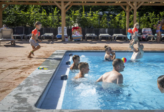 Børn og voksne leger i en udendørs swimmingpool på Veluwecamping De Pampel i Gelderland, Holland.