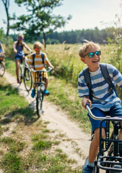 Niños felices montan en bicicleta por un camino de tierra cerca de un parque de vacaciones con glamping.