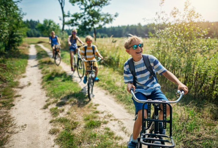 Niños felices montan en bicicleta por un camino de tierra cerca de un parque de vacaciones con glamping.