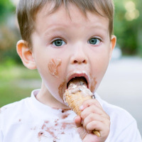 Niño pequeño comiendo un helado, cara y camiseta manchadas, disfruta glamping en un parque de vacaciones.