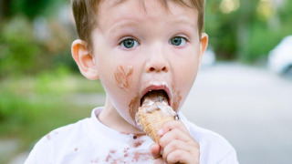 Petit garçon mange une glace, visage et t-shirt tachés, profite du glamping dans un parc de vacances.