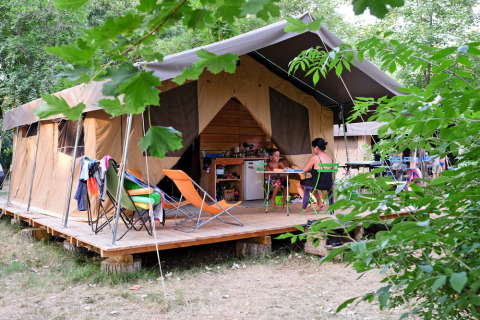 Familia disfruta de glamping frente a tienda en Huttopia Millau, parque vacacional en Occitania, Francia.