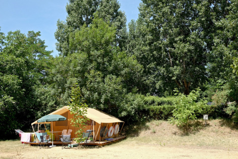 Tienda amarilla y muebles de exterior rodeados de árboles verdes en Huttopia Millau, Occitania, Francia.