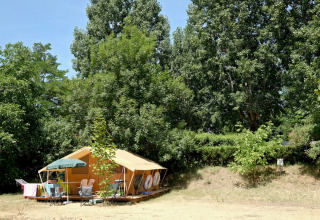 Tenda gialla con arredi da giardino tra alberi verdi a Huttopia Millau, parco vacanze in Occitania, Francia.