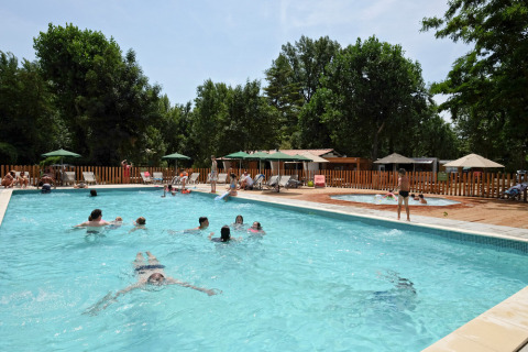 Huéspedes nadando y relajándose junto a la piscina en Huttopia Millau, un parque vacacional en Occitania, Francia.