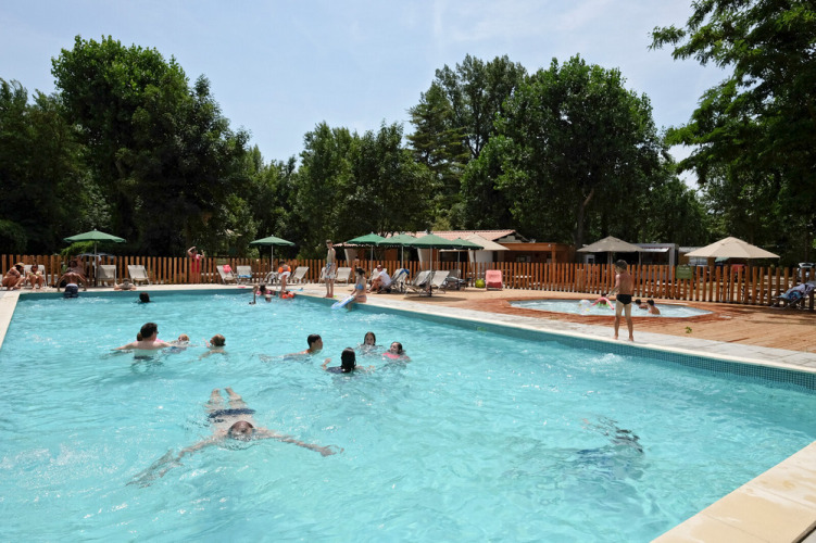 Des vacanciers nagent et se détendent près de la piscine au domaine Huttopia Millau en Occitanie, France.