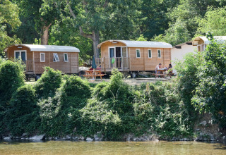 Houten chalets aan het water in vakantiepark Huttopia Millau in Occitanië, Frankrijk, omgeven door groen.