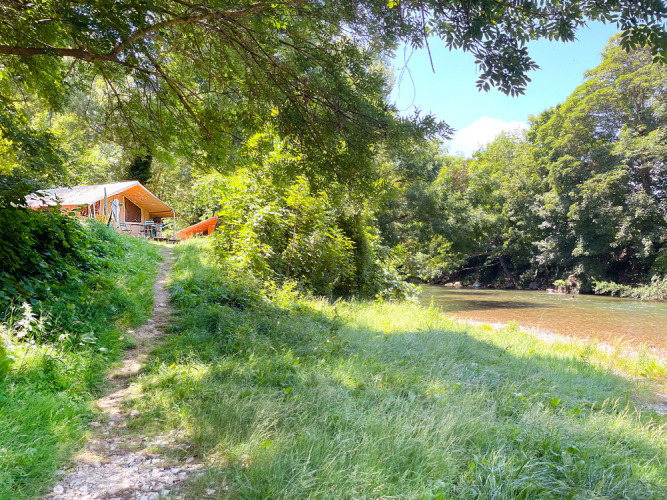 Pathway leading to a tent lodge by the river surrounded by greenery at Huttopia Millau, Occitanie, France.