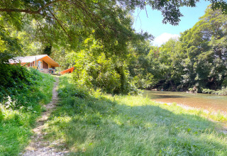 Sendero hacia una cabaña de tela junto al río y rodeada de árboles en Huttopia Millau, Occitania, Francia.