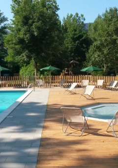 Piscina exterior y zona de spa con tumbonas y sombrillas en Huttopia Millau, Occitanie, Francia.