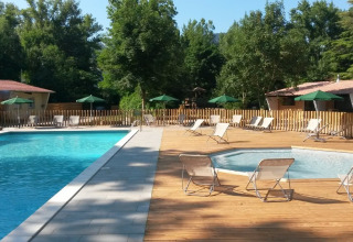 Outdoor swimming pool and spa area with lounge chairs and umbrellas at Huttopia Millau, Occitanie, France.
