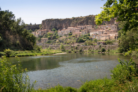 Panorama su un fiume con vegetazione e il villaggio di Millau su una scogliera in Occitania, Francia.