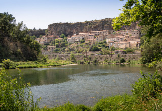 Vue d'une rivière entourée de verdure et du village de Millau perché sur une falaise, Occitanie.