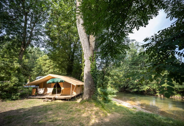 Tent camping by a riverside in lush woods at Huttopia Millau holiday park in Occitanie, France.