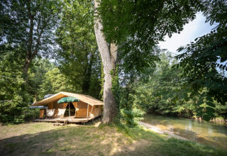 Tent camping by a riverside in lush woods at Huttopia Millau holiday park in Occitanie, France.