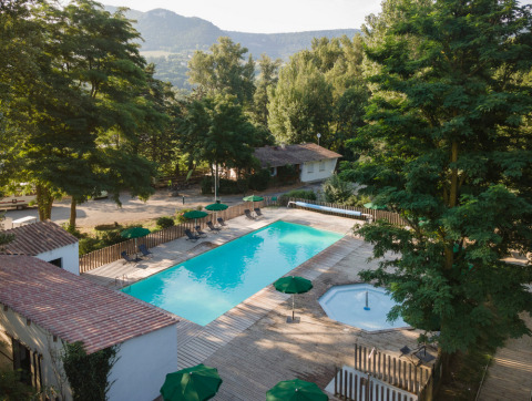 Vista de la piscina y los árboles en Huttopia Millau, un parque vacacional en Occitania, Francia, con montañas al fondo.
