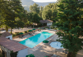 View of the swimming pool and trees at Huttopia Millau holiday park in Occitanie, France, with mountains in background.