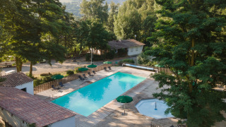 Vista de la piscina y los árboles en Huttopia Millau, un parque vacacional en Occitania, Francia, con montañas al fondo.