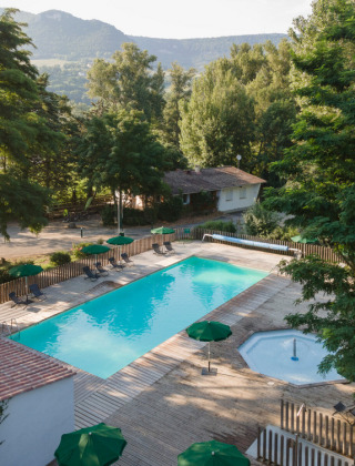 Vista de la piscina y los árboles en Huttopia Millau, un parque vacacional en Occitania, Francia, con montañas al fondo.