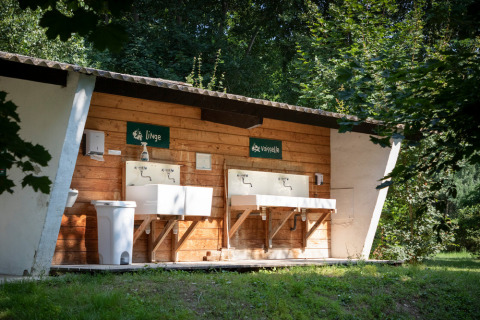 Zona exterior de lavado y fregadero en el parque vacacional Huttopia Millau, rodeado de árboles en Occitania, Francia.