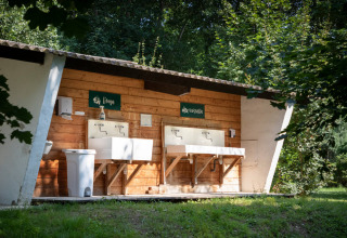 Buitenwas- en vaatwasruimte bij Huttopia Millau vakantiepark, omgeven door bomen in Occitanië, Frankrijk.