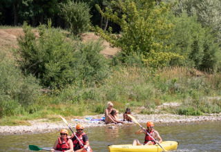 Two people kayak on a river at Huttopia Millau as two others relax on the shore in Occitanie, France.