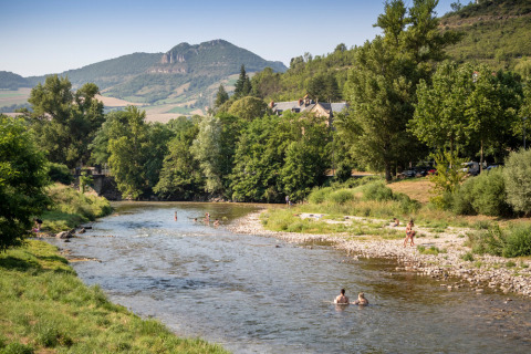 Parque vacacional Huttopia Millau en Occitania, Francia, con río, bañistas y montañas al fondo.